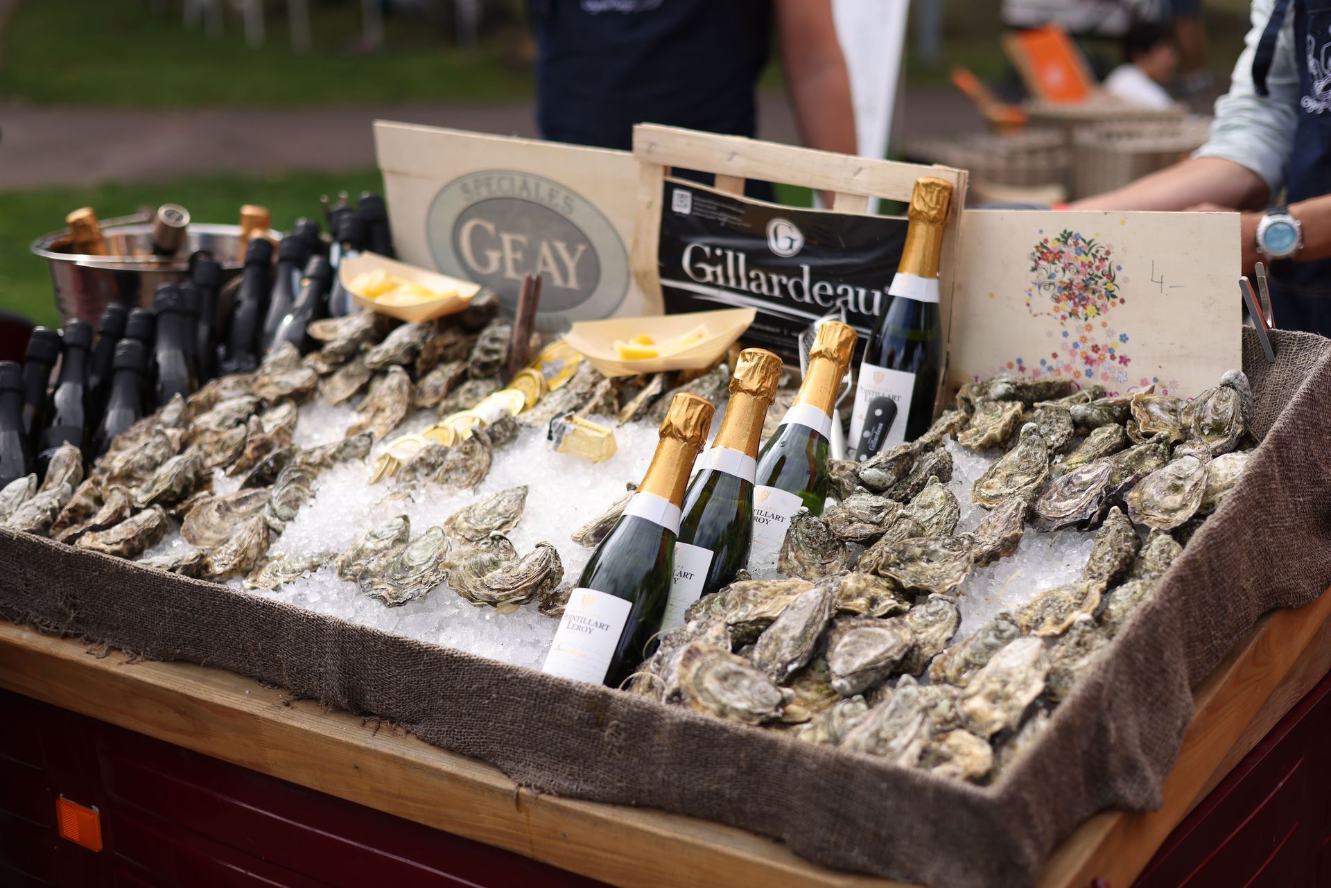 Présentation d'huîtres sur glace pilée avec des quartiers de citron et des bouteilles de champagne sur un étal de marché en plein air