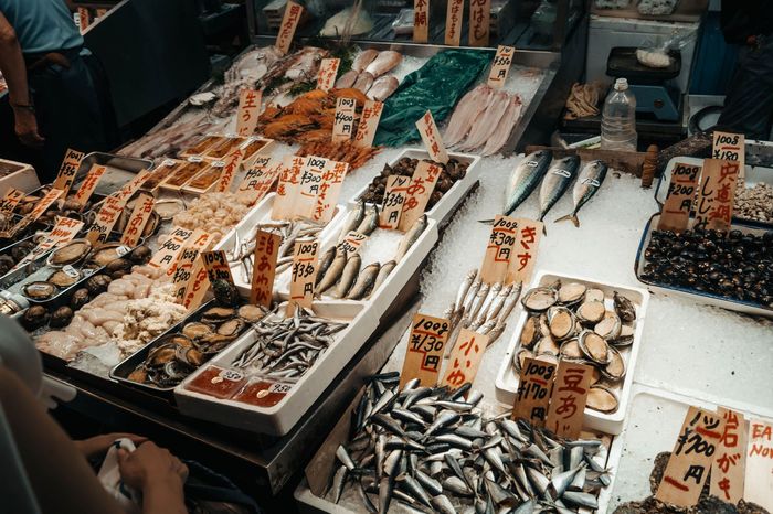Étal de poissonnerie avec des plateaux de poissons et coquillages et des étiquettes de prix écrites à la main