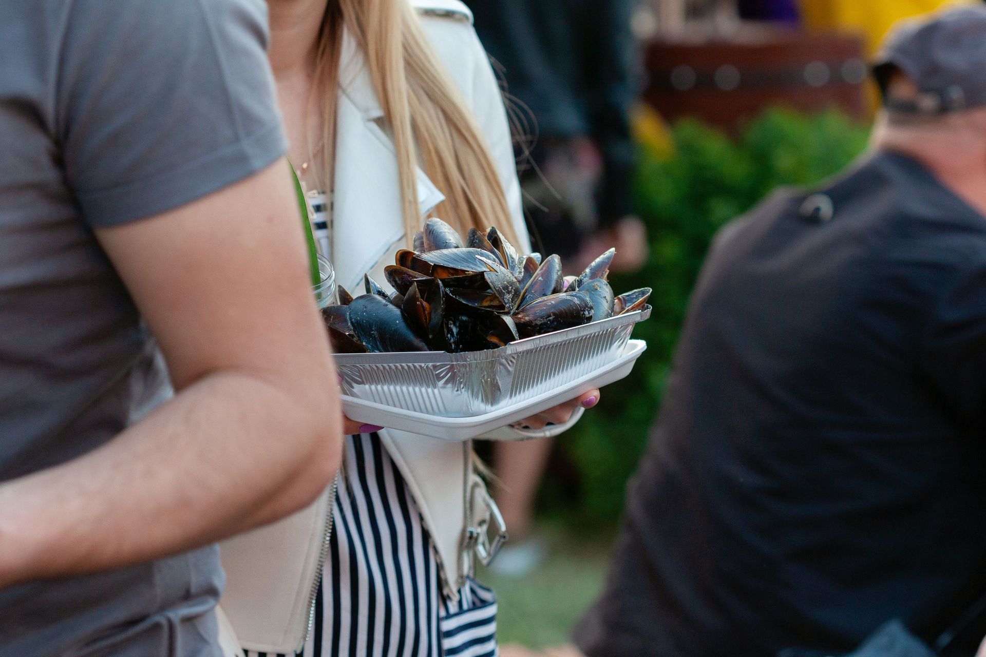 Une personne tenant un plateau de moules lors d'un événement en plein air