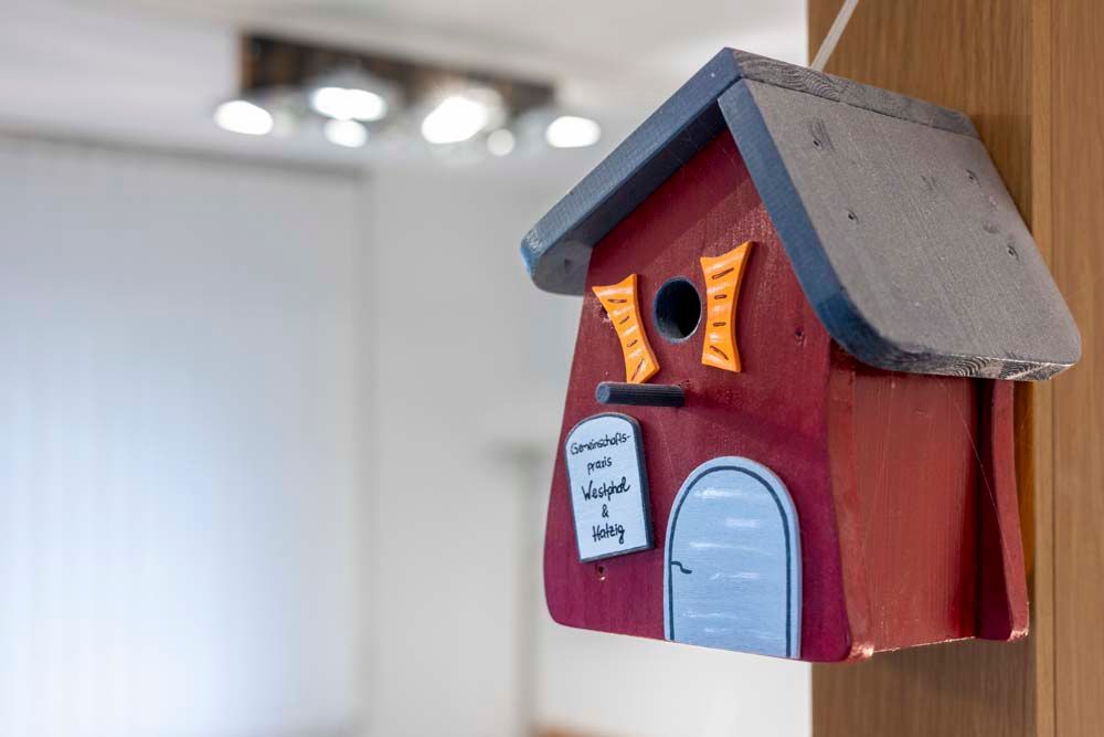 An einem Holzpfosten hängt ein rotes Vogelhaus.