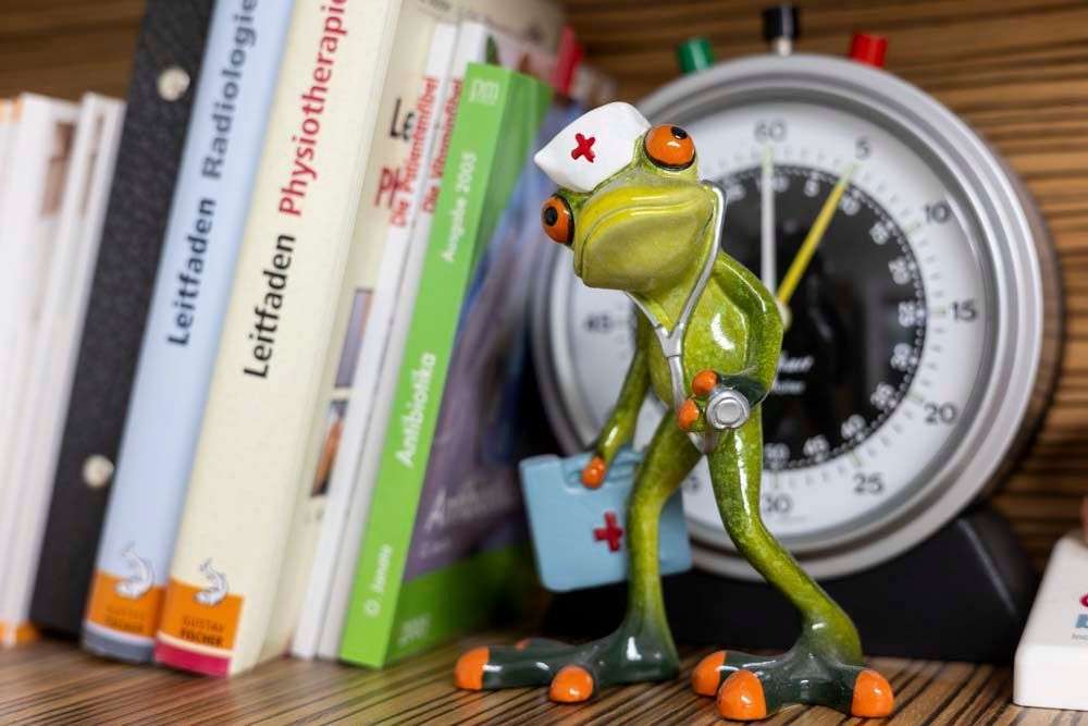 Ein Frosch mit einem Stethoskop um den Hals steht neben einer Uhr und Büchern.