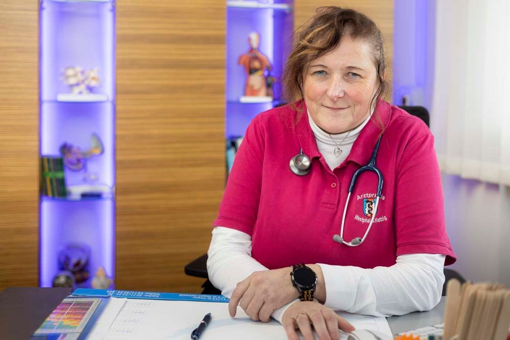 Eine Frau sitzt mit einem Stethoskop um den Hals an einem Schreibtisch.