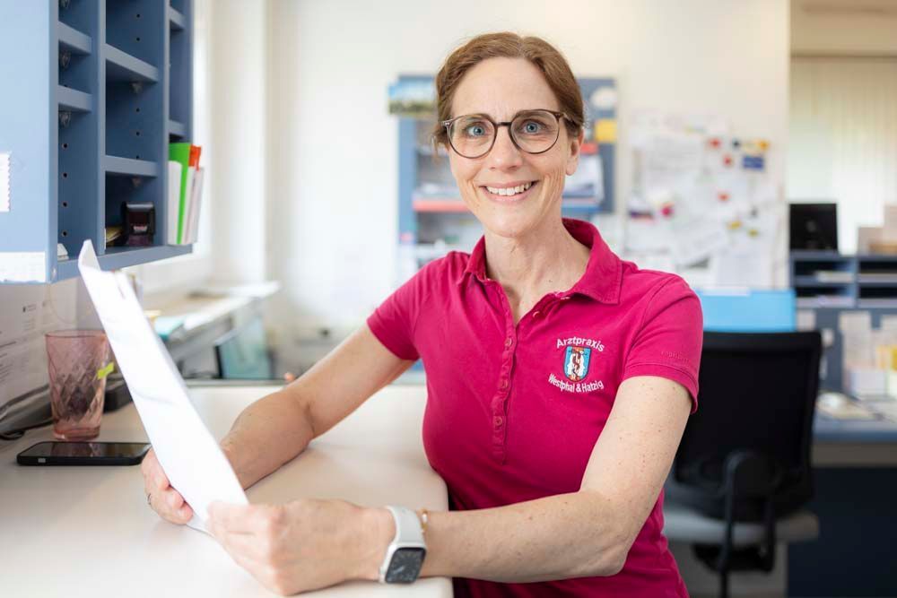 Eine Frau sitzt an einem Schreibtisch und hält ein Blatt Papier in der Hand.