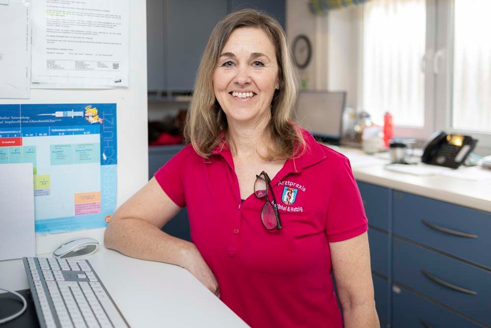 Eine Frau in einem rosa Hemd sitzt an einem Schreibtisch vor einem Computer.