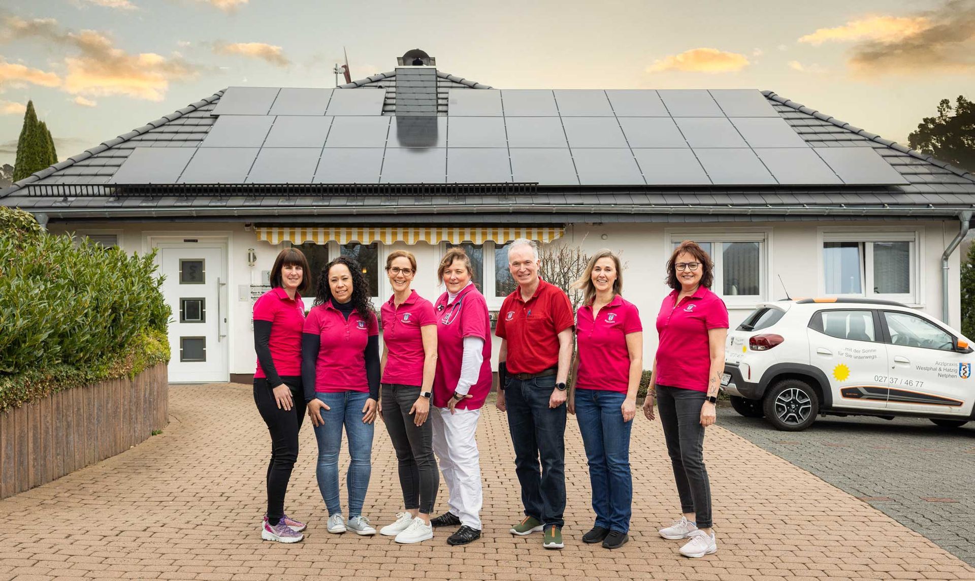 Eine Gruppe von Menschen steht vor einem Haus mit Solarmodulen auf dem Dach.