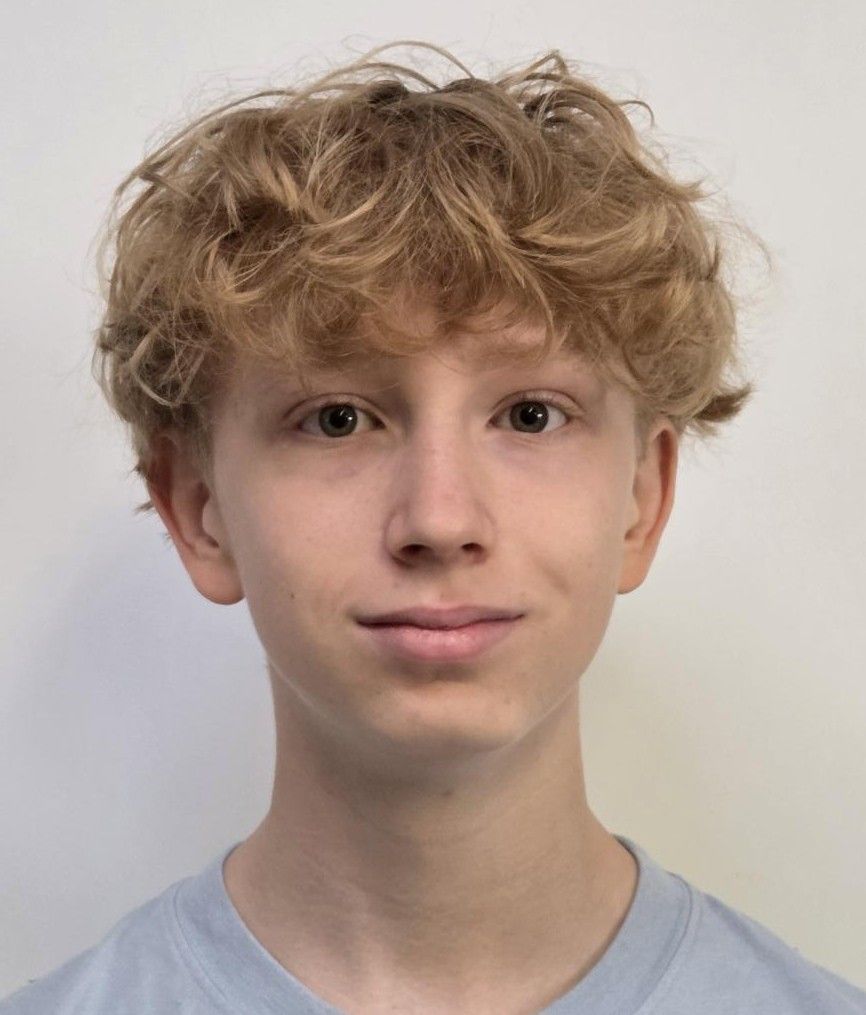 Blonde Person lächelt in einem dunkelblauen Hemd vor weissem Hintergrund.