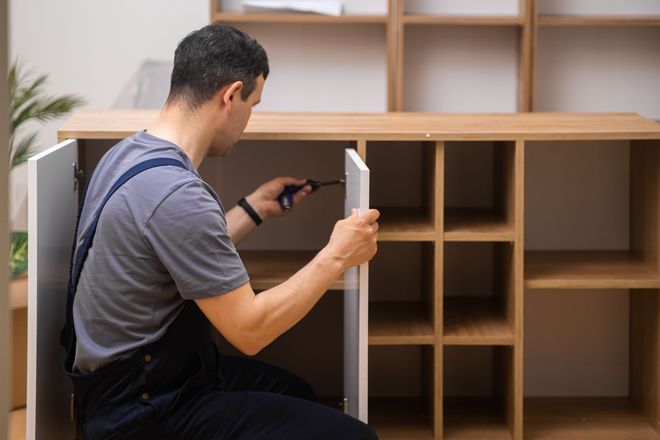 Eine Person montiert mit einem Schraubenzieher einen Holzschrank.