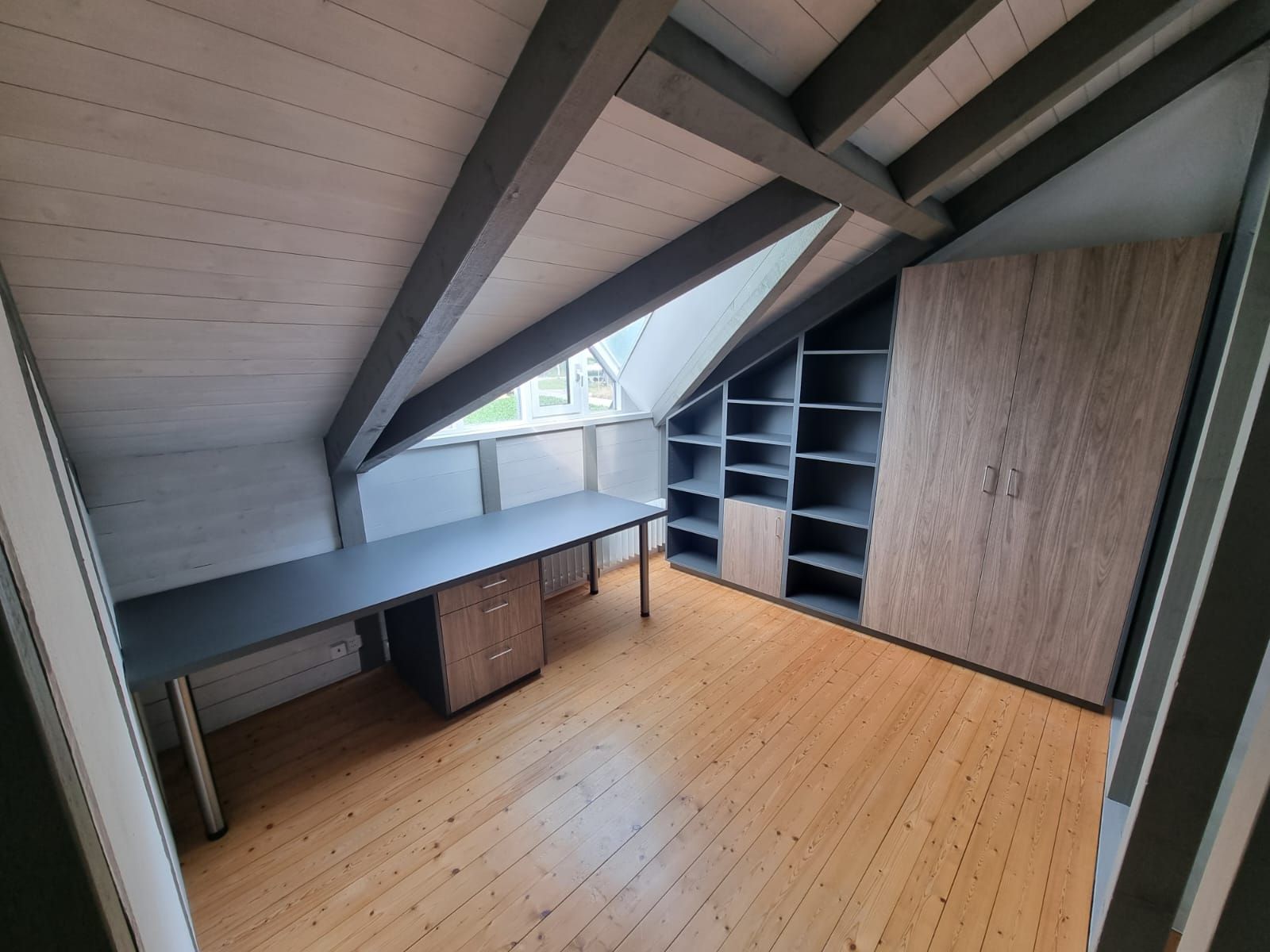 Eine Holzterrasse mit rötlich-braunen Dielen grenzt an ein felsiges Bett und ein modernes Haus mit Glastüren.