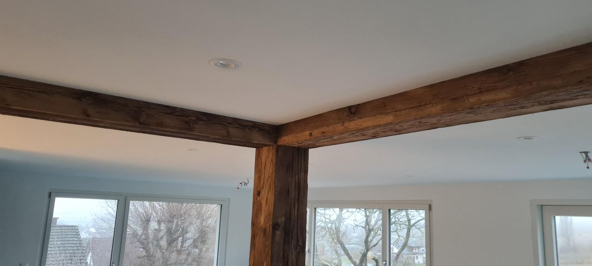 Eine Holzterrasse mit rötlich-braunen Dielen, ausgestattet mit weissen Stühlen und einem Tisch, neben einem weissen Gebäude und Felsen.