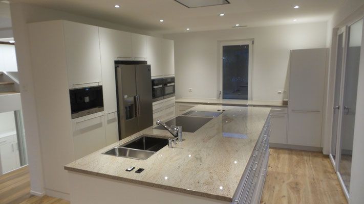 Moderne Küche mit hellem Holzboden, weissen Schränken, grosser Kochinsel, Edelstahlgeräten und Granitarbeitsplatten.