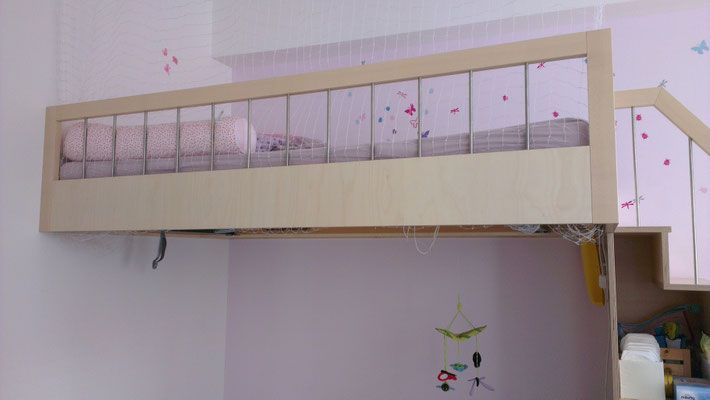 Hochbett mit hellem Rahmen, inklusive Decken und Kissen, an einer rosa Wand befestigt.