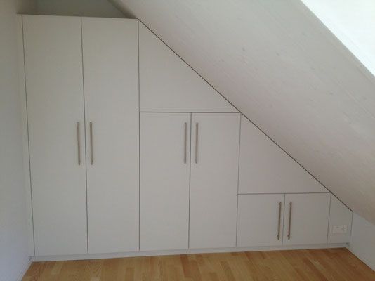 Weisse Einbauschränke wurden in einem Raum mit Dachschräge und Holzboden installiert.