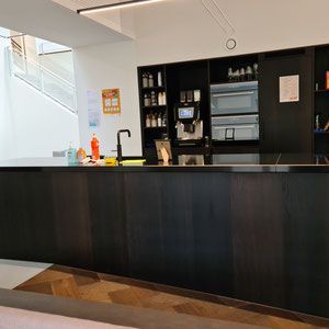 Dunkle Holztheke mit Kaffeemaschine, Schränken und Mikrowelle in einer Büroküche.