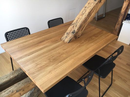 Esstisch aus Holz mit einem baumstammähnlichen Balken, schwarze Stühle, heller Holzboden, modernes Interieur.