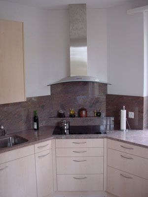 Moderne Küche mit Granitarbeitsplatten, Dunstabzugshaube aus Edelstahl und hellen Holzschränken.