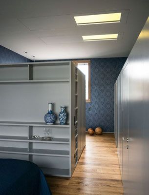 Modernes Schlafzimmer mit Bücherregalen, blau gemusterter Tapete, Holzboden und einem Bett.