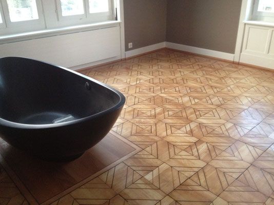 Eine schwarze Badewanne in einem Zimmer mit gemustertem Holzboden und braunen Wänden.