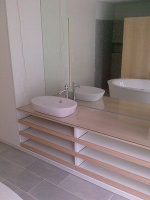 Modernes Badezimmer mit Waschbecken, grosem Spiegel und offenen Regalen. Im Spiegel spiegelt sich eine Badewanne.