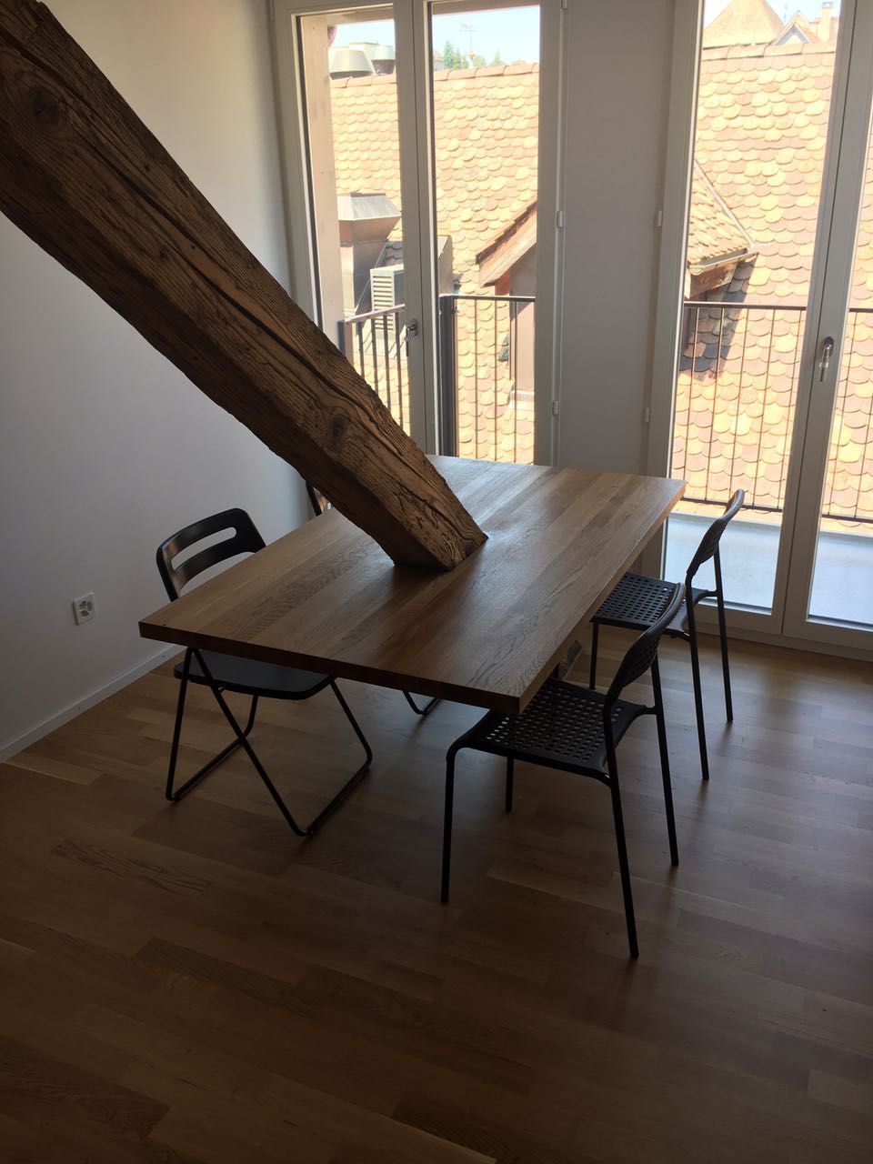 Esszimmer mit Holztisch, schwarzen Stühlen und Holzbalken. Grosse Fenster und Holzböden.