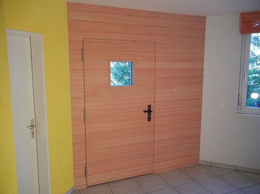 Holztür mit kleinem Fenster in einer getäfelten Wand; weisser Türrahmen links, Fenster rechts; gelbe und weisse Wände.