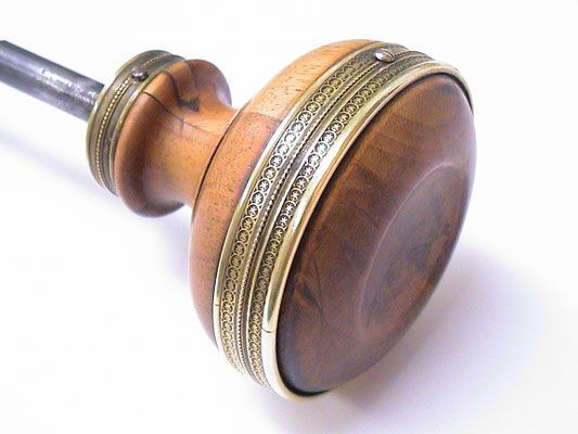 Türknauf aus Holz mit Metalleinfassung und daran befestigter Metallstange.