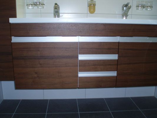 Dunkler Holzwaschtisch mit silbernen Griffen und weisser Arbeitsplatte; gefliester Spritzschutz und Boden.