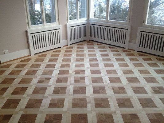 Zimmer mit hellem Parkettboden in Gittermuster. Fenster und weisse Heizkörperverkleidungen säumen die Wände.