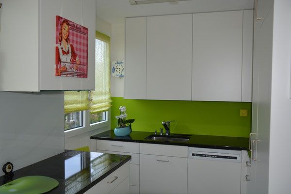 Kleine weisse Küche mit schwarzen Arbeitsplatten, grünem Fliesenspiegel und einem Retro-Kühlschrankmagneten.