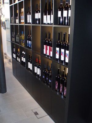 Weinflaschen in Regalen in einem Einzelhandelsgeschäft, mit einer schwarzen Vitrine und neutralfarbigem Boden.