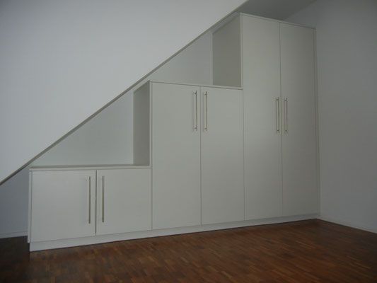 Weisse Einbauschränke unter einer Dachschräge in einem Raum mit Holzboden.