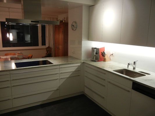 Moderne weisse Küche mit Edelstahlgeräten, Arbeitsplatte und Schränken.