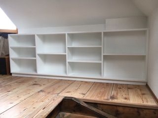 Eingebaute weisse Bücherregale auf einem Holzboden in einem Raum mit Dachschräge.