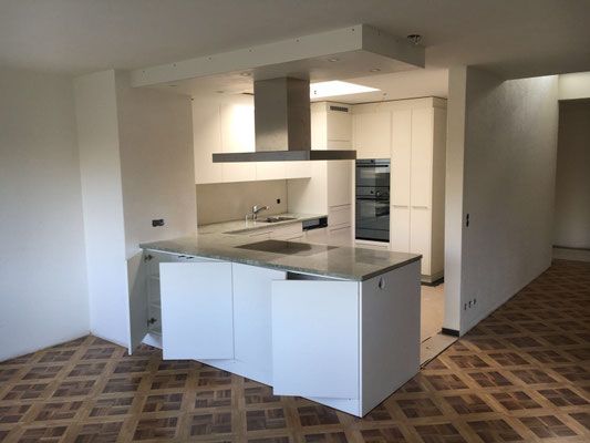 Moderne Küche mit weissen Schränken, Dunstabzugshaube aus Edelstahl und Kücheninsel mit Granitarbeitsplatte.