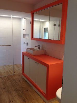 Badezimmer in Orange und Weiss mit Waschtisch, Spiegelschrank und Glasdusche.