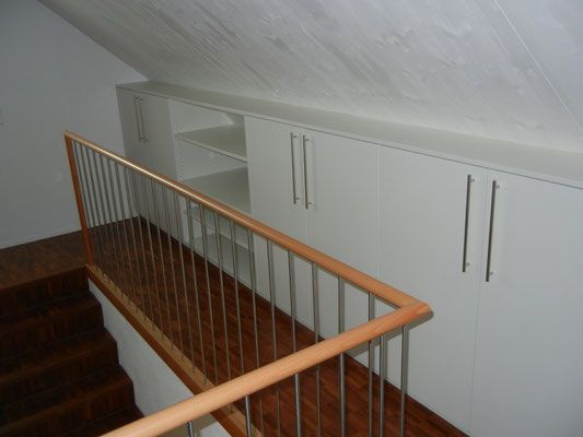 Treppe mit Holzstufen und Geländer. Weisse Einbauschränke in der Dachschräge.