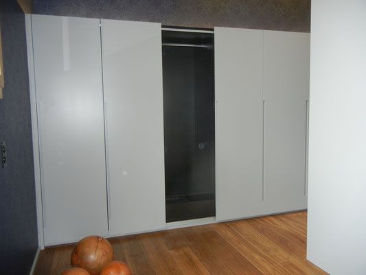 Weisser Schiebetürenschrank mit offenem Bereich, hinter dem hängende Kleidung sichtbar ist, auf Holzboden.