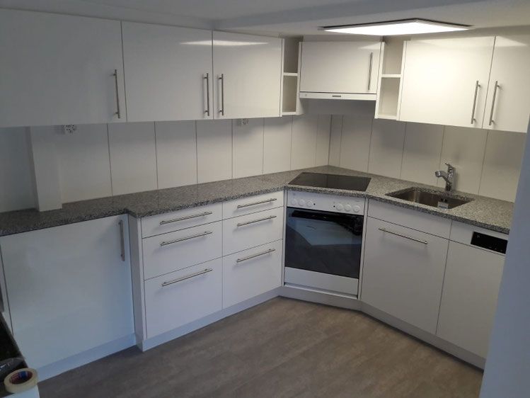 Weisse Küchenschränke mit Granitarbeitsplatten, Backofen, Spüle und Kochfeld.