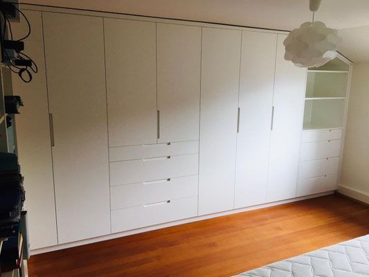 Weisser Einbauschrank mit mehreren Türen und Schubladen in einem Schlafzimmer mit Holzboden.