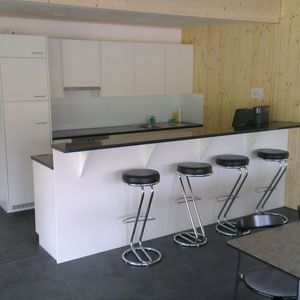 Moderne weisse Küche mit schwarzer Arbeitsplatte und Barhockern.