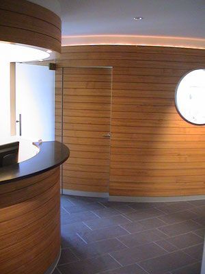 Empfangsbereich mit Holzvertäfelung, geschwungenem Empfangstresen, rundem Fenster und Tür.