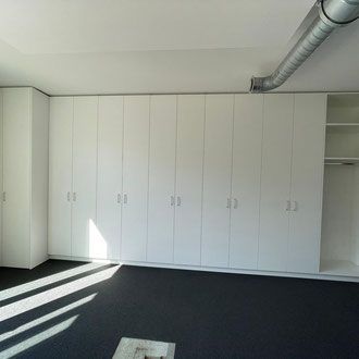 Weisse Schranktüren an einer Wand in einem Zimmer mit dunklem Boden und einem freiliegenden Metallrohr.