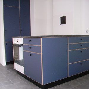 Blaue Küchenschränke mit schwarzen Arbeitsplatten und schwarzen Knöpfen; eingebauter Backofen.