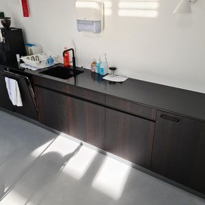 Ein dunkler Holzschrank mit schwarzer Arbeitsplatte beherbergt ein Spülbecken und Zubehör in einer Küche.