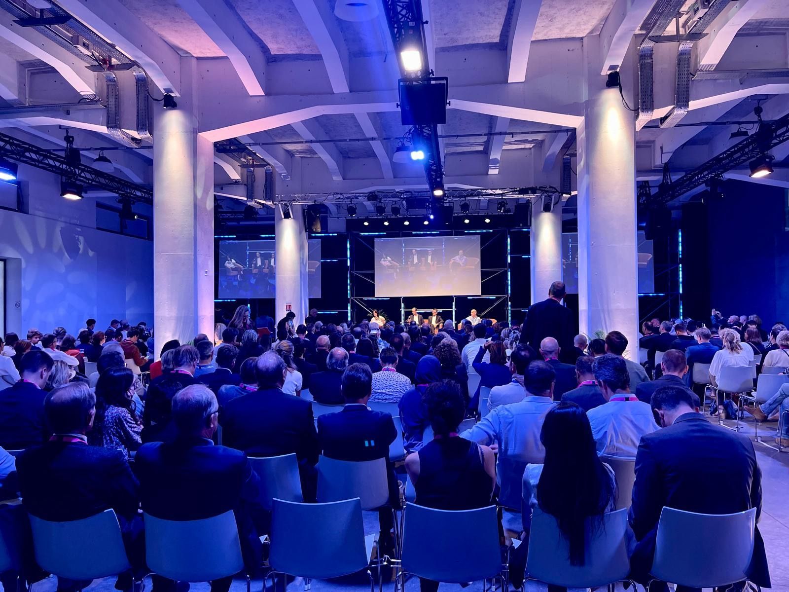 Audience seated in a blue-lit conference hall facing a presentation screen for MEDEF ça match event