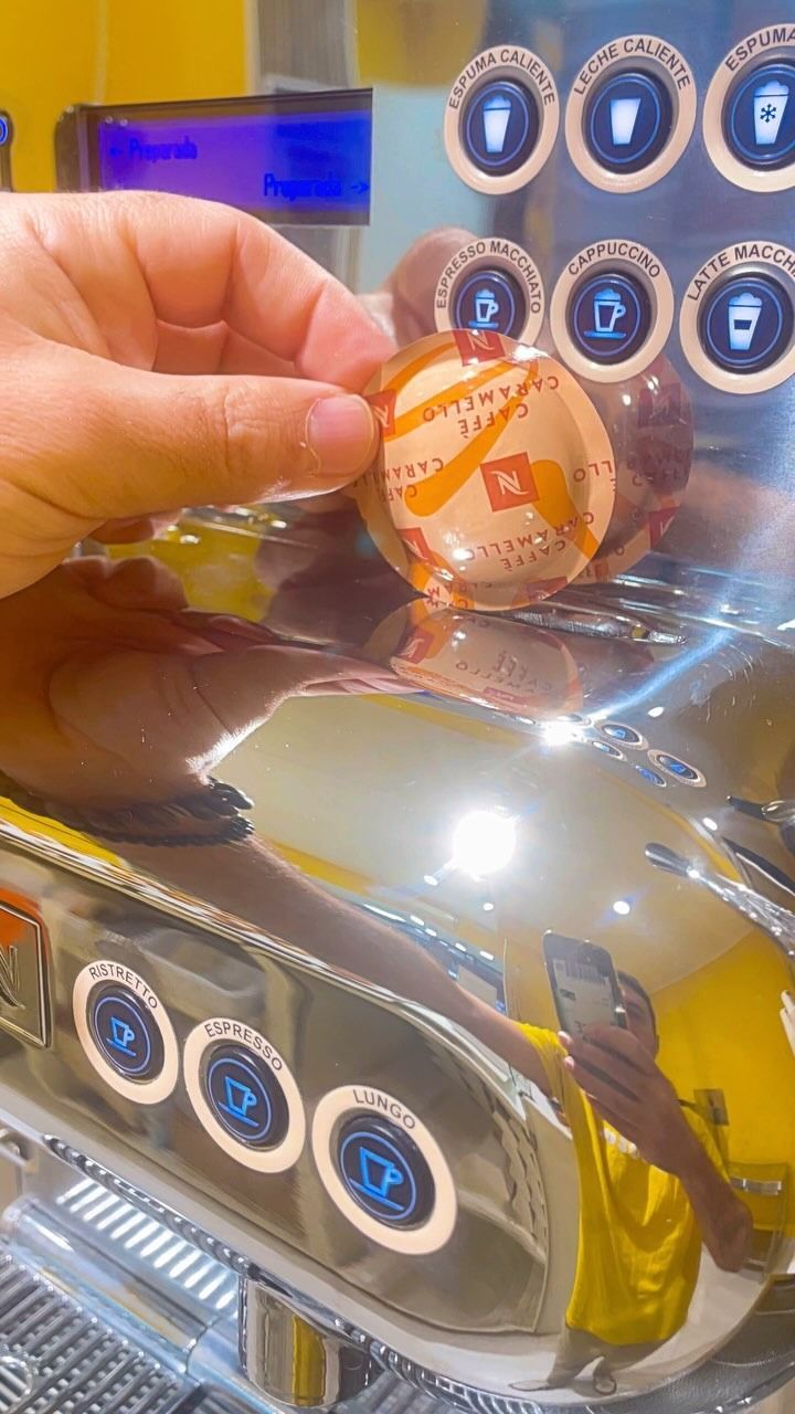 Una persona sostiene una cápsula de café delante de una máquina de café.