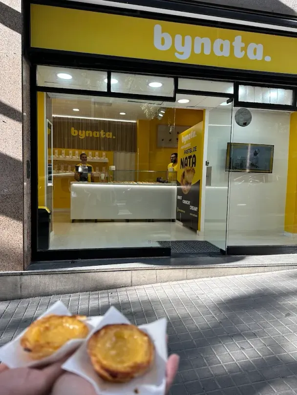 Una persona sosteniendo dos pasteles frente a una tienda Bynata.