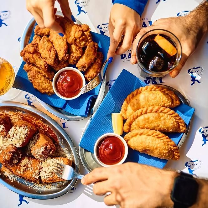 Variedad de alimentos fritos y salsas para mojar sobre una mesa, con manos que se extienden hacia ellos.