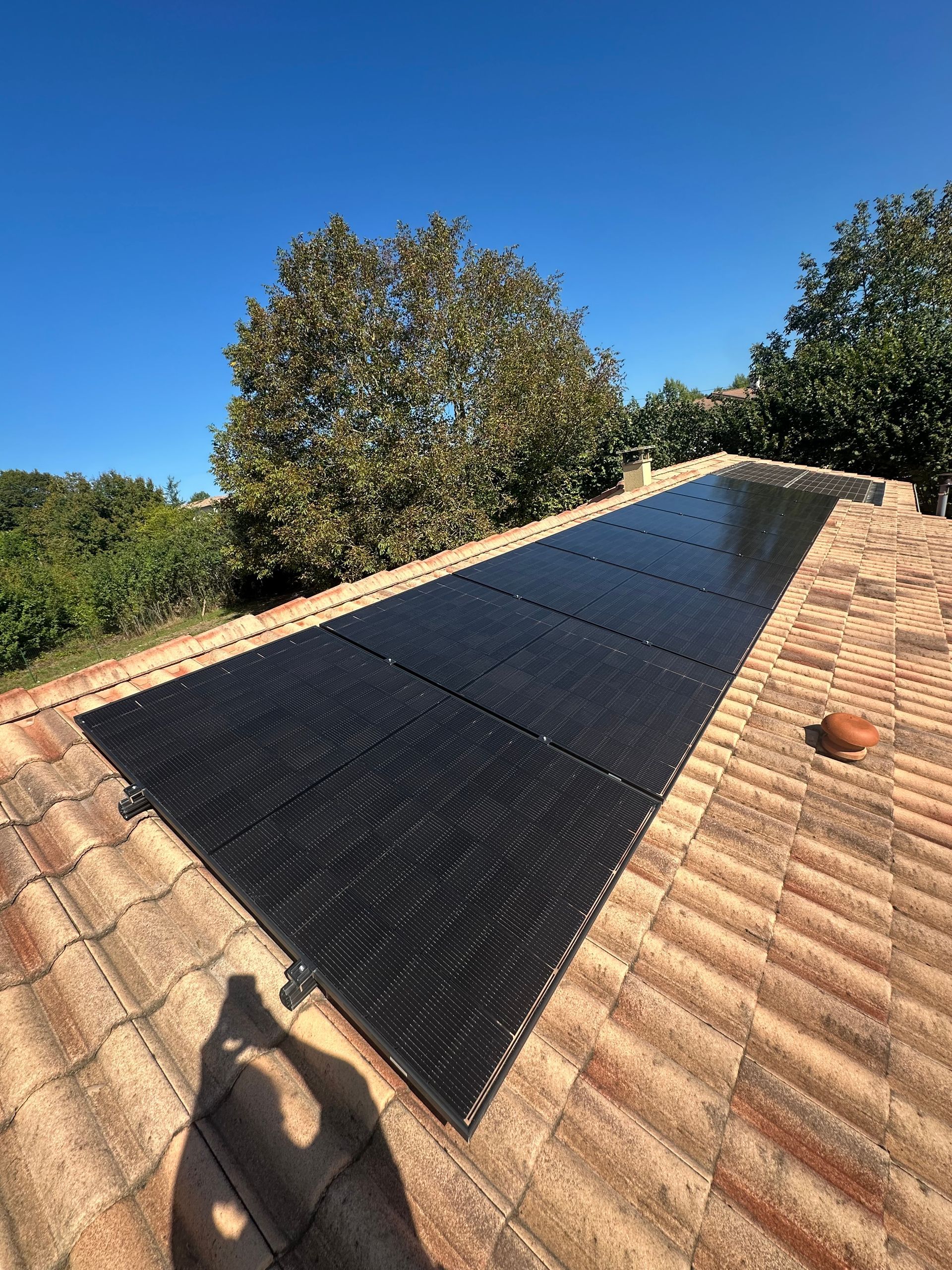 Un tapis chauffant solaire noir pour piscine, installé sur un toit de tuiles en terre cuite, sous un ciel bleu azur.