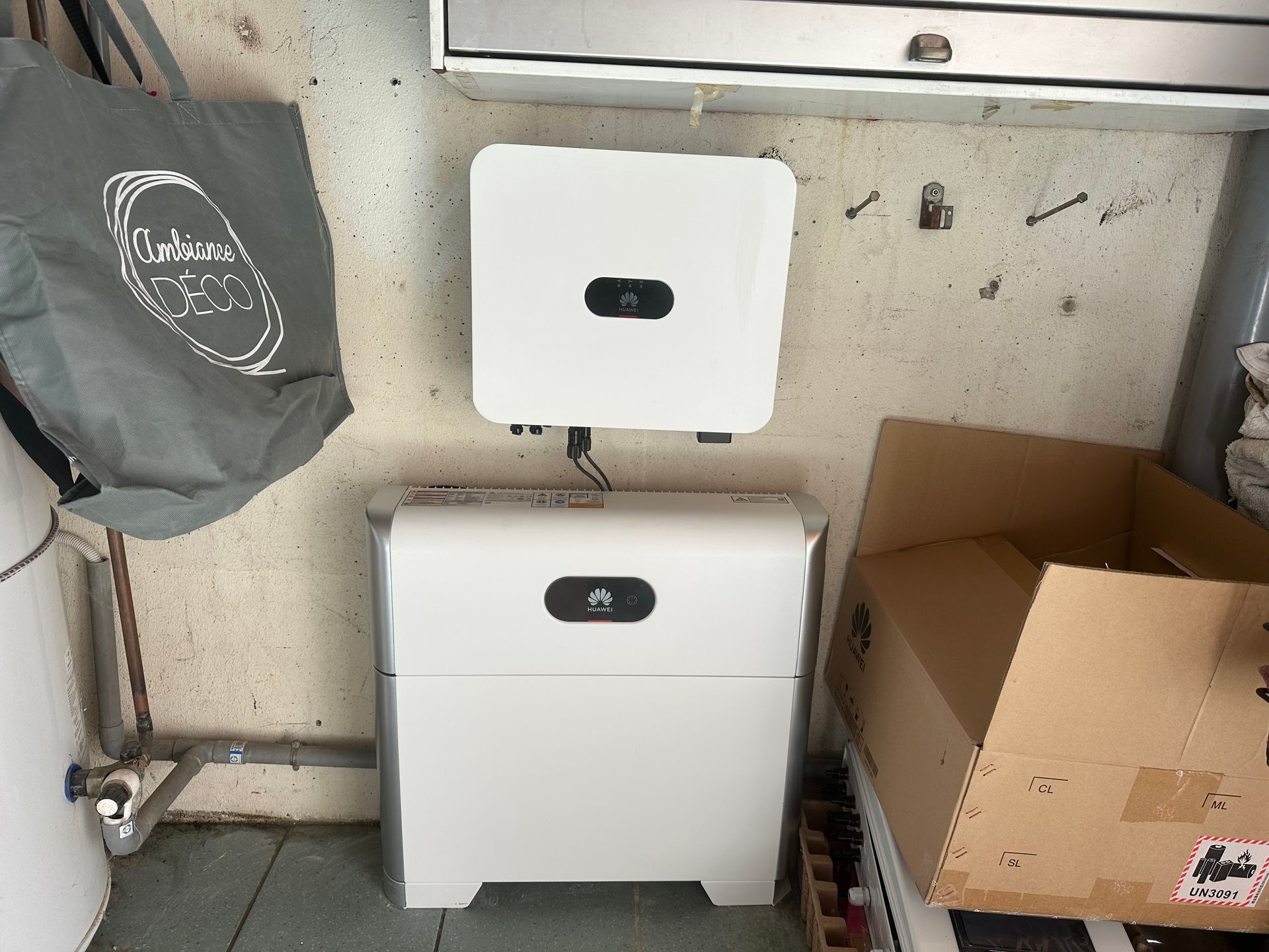 Un onduleur solaire Huawei blanc fixé au mur, positionné au-dessus d'une unité de stockage de batterie résidentielle blanche dans une pièce.