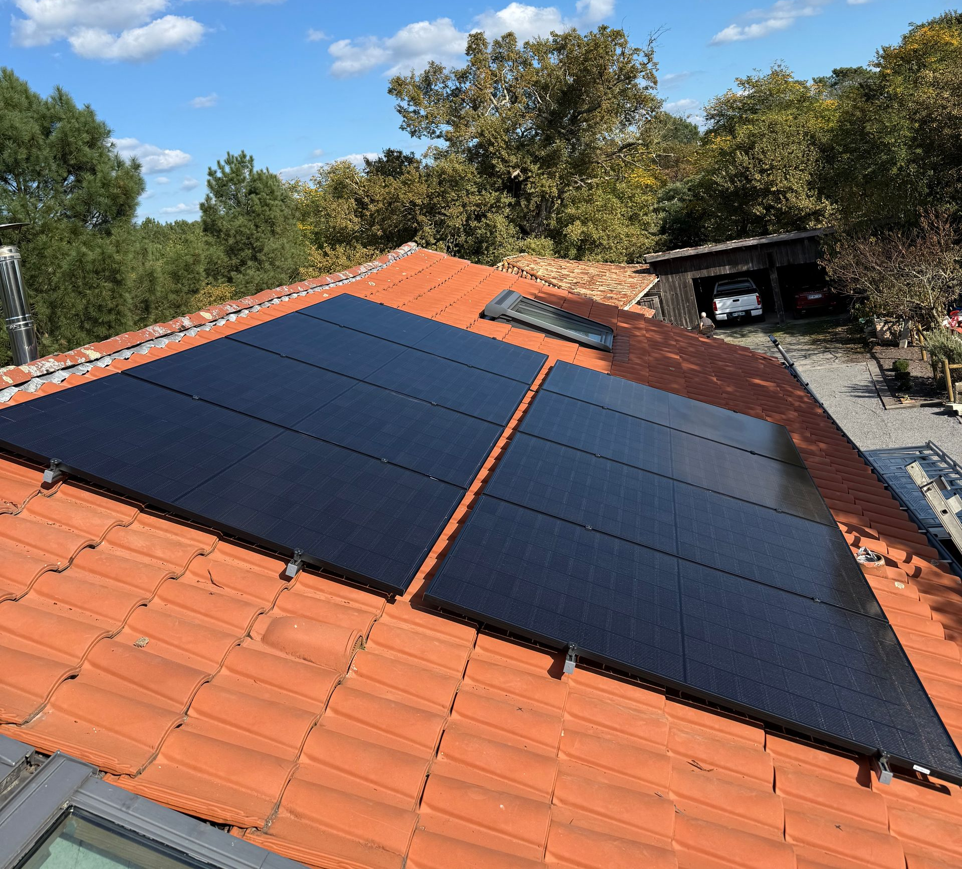 Deux rangées de panneaux solaires rectangulaires noirs, installées sur un toit en pente recouvert de tuiles en terre cuite orange, sous un ciel bleu.